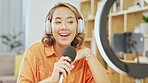 Media, podcast and smile, asian woman with microphone in living room streaming, recording or broadcast from home studio. Video, webinar and vlogging, happy influencer on live stream internet channel.