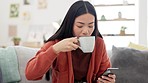 Coffee, phone and Asian woman on a sofa browsing on social media, mobile app or the internet. Relax, technology and female drinking a cappucino while scrolling on cellphone in the living room at home