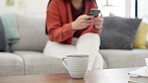 Coffee, relax and table with a woman in the background of her home living room typing a text message. Tea, cup and beverage with a mug on a wooden surface in the room of a house interior closeup