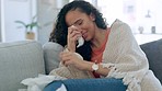 Crying, depression and sad woman on a living room sofa with a tissue and mental health problem. House, anxiety and suffering of a mixed race female on a home lounge couch with tissues in distress