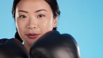 Boxing gloves, face and woman punching in studio, blue background and sports challenge. Portrait, female model and asian boxer fighting for fitness, mma exercise and workout power for action training