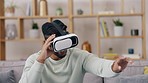 Virtual reality, metaverse and man in the living room with a headset while playing a 3d video game. Futuristic, innovation and male gamer sitting on a sofa while gaming with vr goggles in his home.