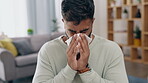 Covid, blowing nose and allergies with a man in his home feeling sick, ill or unwell in the living room. Healthcare, tissue and sneezing with a young male suffering from a virus infection in a house