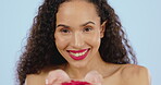 Smile, face and woman blowing confetti in studio, blue background and color backdrop. Portrait of happy female model celebrate with red glitter, love and romance for valentines day beauty celebration