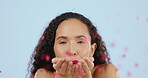 Portrait, flowers and valentines day with a black woman blowing petals in studio on a blue background. Face, love and romance with an attractive young female indoor to celebrate passion or affection