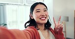 Face, woman and peace for selfie in home, smile and fun with live streaming vlog in living room. Portrait, profile picture and happy asian female show v sign, hand emoji and happiness on social media