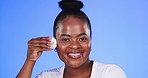 Face, black woman and cotton pad to remove makeup, grooming and girl against a blue studio background. Portrait, African American female and happy lady with cosmetics product, skincare or smooth skin
