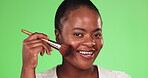 Black woman, makeup brush and face portrait for beauty and cosmetics for a glow and shine in studio. Happy aesthetic female model on a green background for facial self care and skincare with a smile