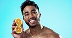 Happy, orange and face of man in studio for skincare, wellness and citrus treatment on blue background. Fruit, facial and portrait of indian male model excited for organic vitamin c skin cosmetics