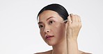 Asian woman, dropper and keratin on face for beauty, skincare or cosmetics against white studio background. Happy female model applying oil drop to skin for hydration, moisturizer or facial treatment