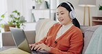 Laptop, headphones and asian woman on couch with work from home opportunity in online or website copywriting. Remote worker or person in china typing on her computer and listening to music at home