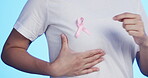 Pink ribbon, breast cancer and awareness with a man in studio on a blue backgroung for health. Chest, medical and healthcare with a male placing a bow, symbol or sign of recognition in october