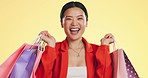 Happy, face and woman in studio with shopping, bag and boutique sale on yellow background. Portrait, excited and asian girl shopper customer with items for discount, fun and retail while isolated