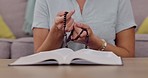 Closeup, hands and woman with rosary, praying and spiritual guidance in living room, hope and peace. Zoom, hand and bible with holy beads, prayer and worship with gratitude, trust and help in lounge