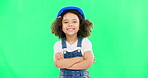 Little girl, face and smile in construction on green screen with safety helmet and arms crossed against a studio background. Portrait of small and happy child architect smiling on chromakey mockup
