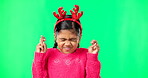 Child, christmas and wish on green screen fingers crossed and antlers for motivation. Girl kid or eyes closed emoji for hope, praying or miracle on studio background space with reindeer headband 