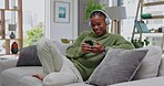 Relax, sofa and black man with phone and headphones in living room listening to podcast streaming service. Smile, music and technology, happy person at home with smartphone, online radio app and wifi