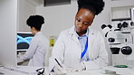 Scientist, microscope and black woman writing research, results or information in lab. Science, notebook and happy female medical doctor write notes for microscopic particle experiment with equipment