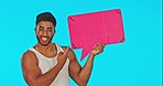 Pointing, speech bubble and face of a man in a studio with mockup space for advertising or marketing. Happy, smile and portrait of an Indian male model showing cardboard mock up by a blue background.