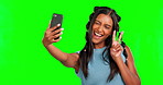 Peace, selfie and a girl with tongue out on a green screen isolated on a studio background. Happy, funny and an influencer woman taking a photo with a hand gesture and silly facial expression
