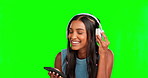 Green screen, headphones and woman on her phone listening to music with mobile app isolated on studio background. Face of gen z indian person typing on cellphone and happy with audio streaming tech