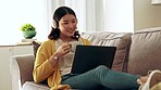 Coffee, laptop and Asian woman on couch, headphones and relax in home, calm and watching video. Japan, female and happy  lady with headset, device and tea in living room, happiness and social media