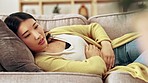 Pain, period and Asian woman with hands on stomach for pregnancy, menstruation or abdominal cramps. Health, digestion problem and girl on sofa holding abdomen for endometriosis, pms and ache at home