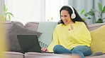 Video call, woman and wave on a sofa in living room with happiness and communication at home. Computer talk, headphones and happy young female with a smile from web and pc conversation in a house