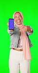 Portrait, green screen and a muslim woman pointing to a phone with tracking markers for marketing. Social media, ecommerce and chromakey with an islamic female showing a mobile screen or display