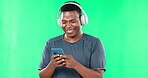 Music headphones, phone and black man laughing on green screen in studio isolated on a background. Cellphone, funny and happiness of African person streaming or listening to podcast, radio or audio.