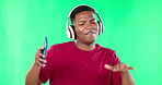 Music headphones, phone and black man dancing on green screen in studio isolated on a background. Cellphone, singing and happiness of African person streaming or listening to podcast, radio or audio.