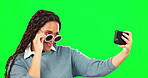 Selfie, sunglasses and smile with a woman on a green screen background in studio for a profile picture. Photograph, fashion and happy with a cool young female posing for social media status update