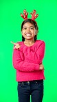 Child, christmas and pointing at space on green screen with finger or hand. Smile portrait of excited girl kid on studio background with antlers headband for holiday celebration mockup with hands