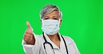 Old woman doctor, mask and thumbs up on green screen with covid, healthcare compliance and safety from virus. Female physician, PPE with corona and agreement with health policy on studio background