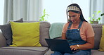 Asian woman, laptop and relax on living room sofa for social media, email or communication at home. Happy female sitting on lounge couch with computer browsing, scrolling or online research indoors