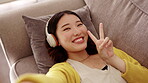 Top view, selfie and Asian woman on couch, peace sign and smile in home, relax and social media. Portrait, Japanese female and lady on sofa, v gesture and headphones in lounge, happiness and cheerful