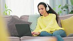 Laptop, writing and woman with headphones on a living room sofa in a home. Music, internet working and computer of a female student listening to a web song on a lounge couch in a house typing