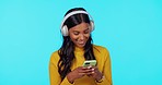 Woman, music and headphones with phone in studio for listening, relax and texting on social media. Gen z girl, smartphone and chat with smile for streaming, audio and search on app by blue background