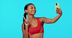 Fitness, woman and peace sign in studio for selfie, profile picture or workout vlog against a blue background. Happy, fit and sporty female smiling for photo, social media or online post on mockup