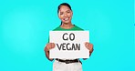 Young woman, go vegan poster and protest by blue background with smile on face for health, diet and ecology. Volunteer, activist and sign on paper board for animal kindness, change or food innovation