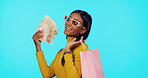 Sales, money and woman with bags, shopping and excited for discount against blue studio background. Female shopper, buyer or person with cash, deals and wealth with boutique items, products and smile