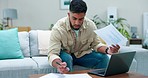 Stress, debt and man with documents and laptop on a sofa for budget, savings and anxiety from financial crisis. Paper, bills and frustrated indian guy checking invoice, payment and  balance in lounge