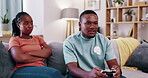 Couple, annoyed and a man gaming in the living room of his home while his girlfriend sits angry on the sofa. Unhappy wife, frustrated and a gamer boyfriend in the house playing an  online video game