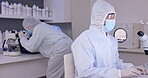 Scientist team in laboratory, PPE and typing at computer, science study for medical research collaboration. People work together, data analysis with microscope and test results on tablet with biotech