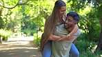 Love, nature and piggy back for interracial couple walking in garden and bonding on summer weekend together. Happiness, man carrying happy woman with smile and laugh on fun, romantic date in park.