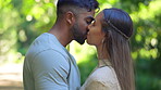 Happy young couple kissing in park for love, care and romance on anniversary date together. Man, woman and kiss partner in affection, support and freedom to relax in sunshine, garden or smile outdoor