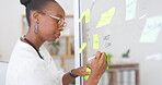 Black woman, writing and planning business schedule on sticky note, glass board or tasks at office. African American female employee in brainstorming, strategy or ideas for project plan at workplace