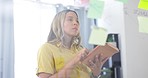 Woman, tablet and planning for business schedule, tasks or project reminder on glass board at office. Female employee working on technology and sticky note for brainstorming or strategy at workplace