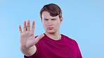 Stop, hand and face of a man in a studio with a moody, upset or angry facial expression. Fear, annoyed and portrait of a serious male model from Canada with a wait gesture isolated by blue background
