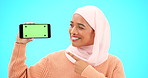 Islam, phone or green screen and a woman on a blue background in studio holding a display with tracking markers. Muslim, mobile contact and an attractive young female showing a screen for marketing